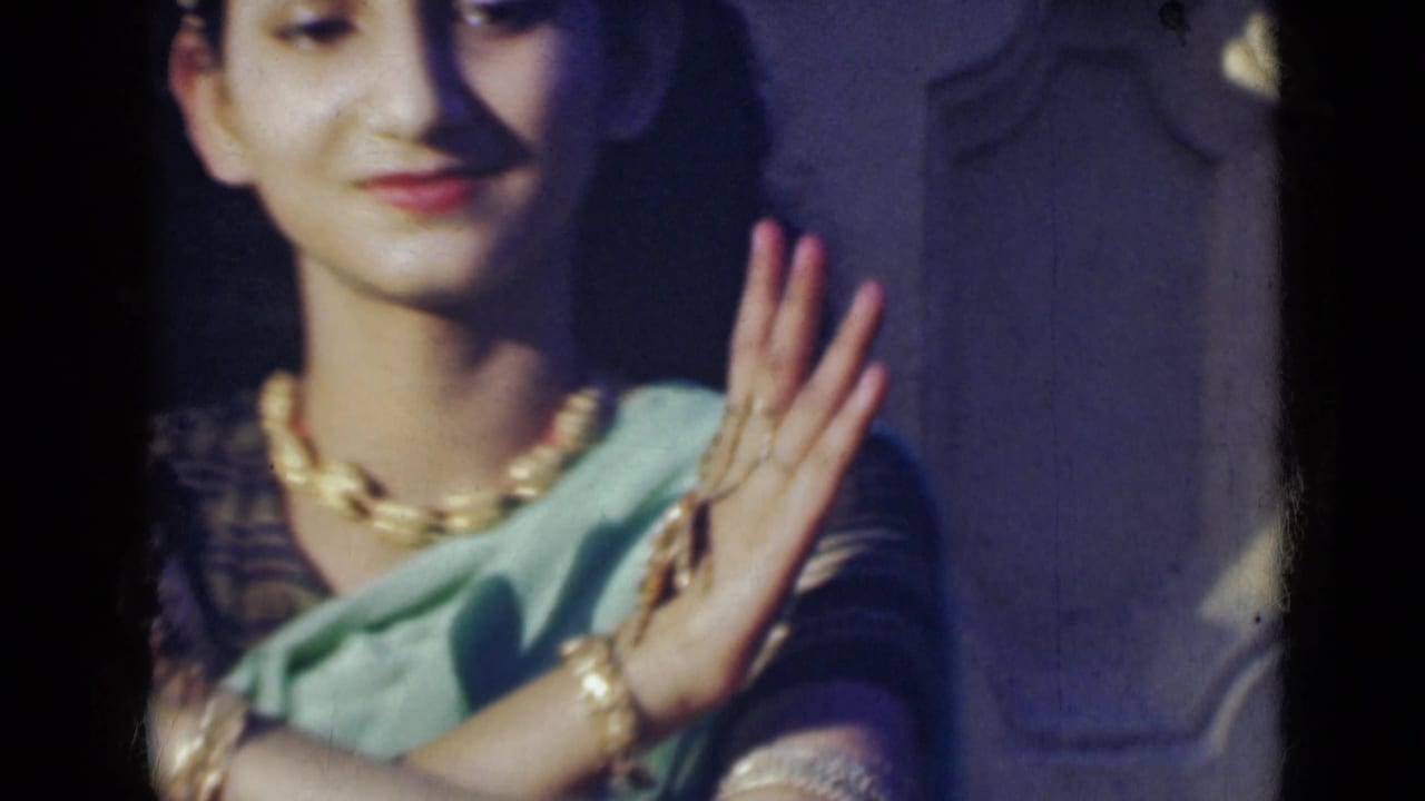 Young woman in sari holds both hands together near her shoulder.