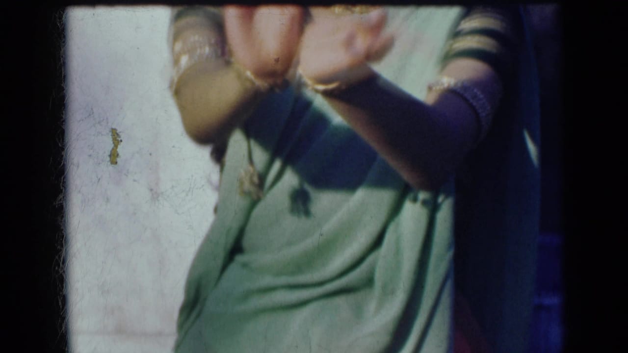 In 1947 India home-movie footage, a cropped woman in a green sari lifts bangle-covered hands during a gesture.