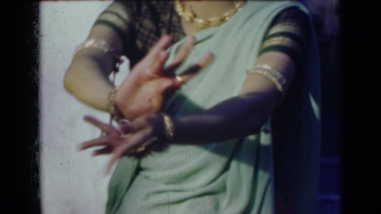 A woman in a green sari extends both hands in a traditional-looking gesture, with jewelry visible on her arms.