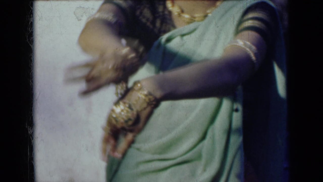 The cropped performer’s bangle-covered hands blur slightly as they move downward across the sari.
