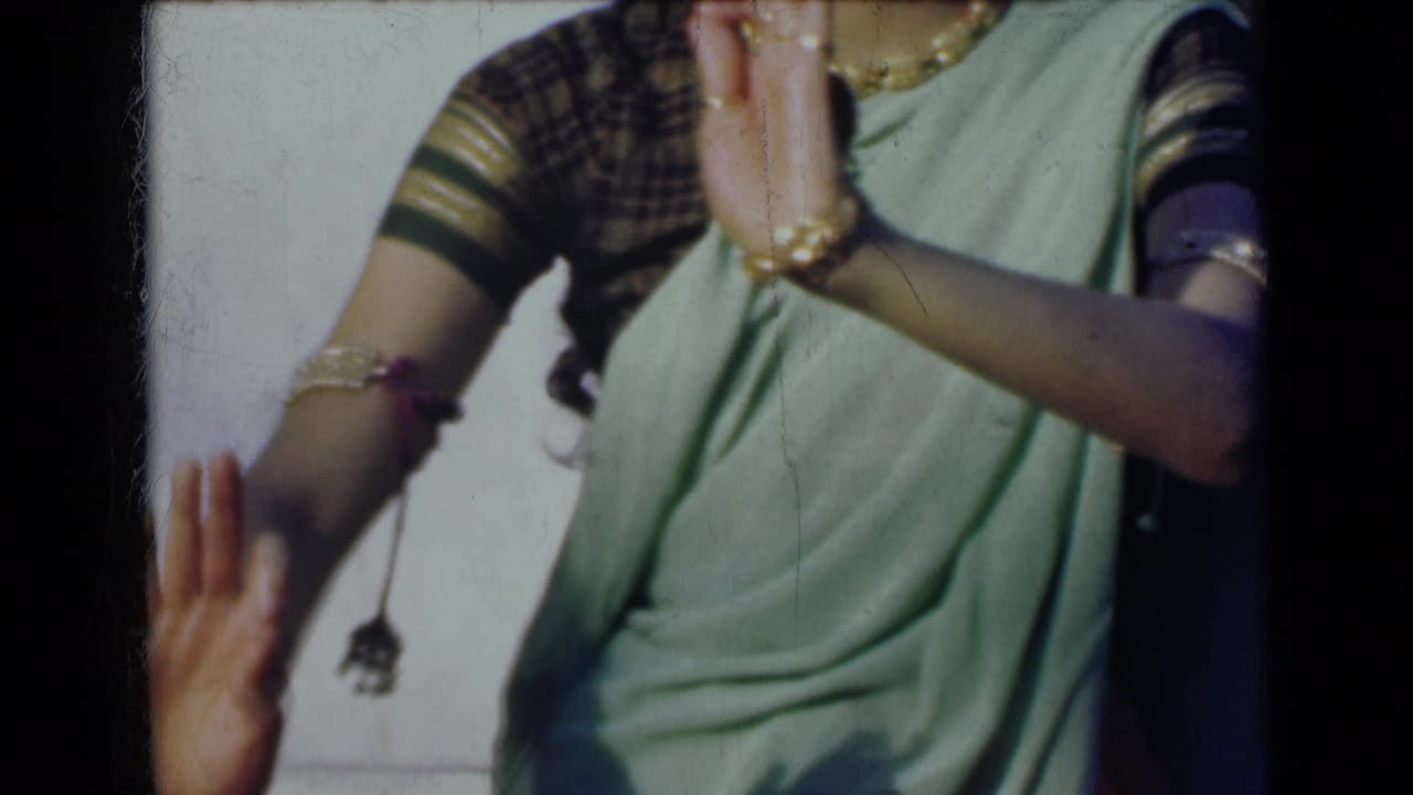 Woman in a light green sari raises both hands, with jewelry visible on her wrists and fingers.