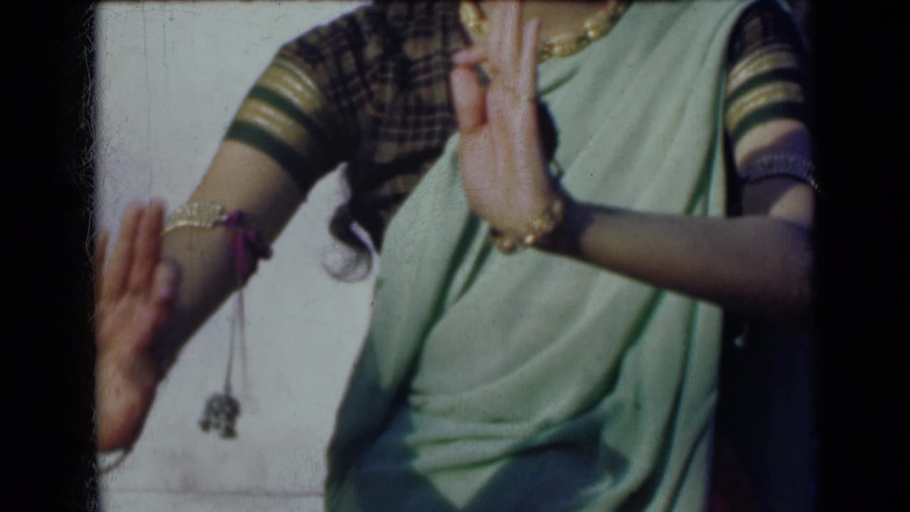 Close view of a woman's raised hands, sari, blouse sleeve, and dangling wrist ornament.