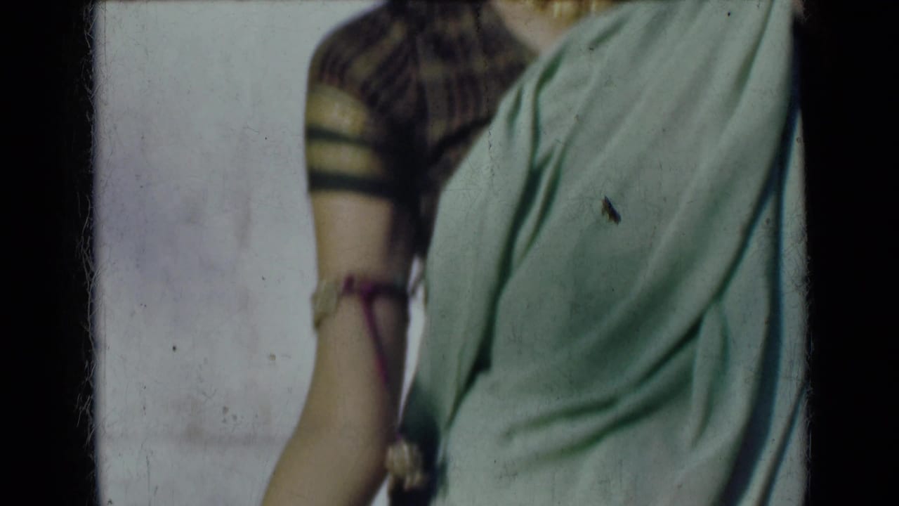 1947 India 8mm frame showing the woman's sari and patterned blouse in a cropped torso view, with one arm lowered and jewelry visible.