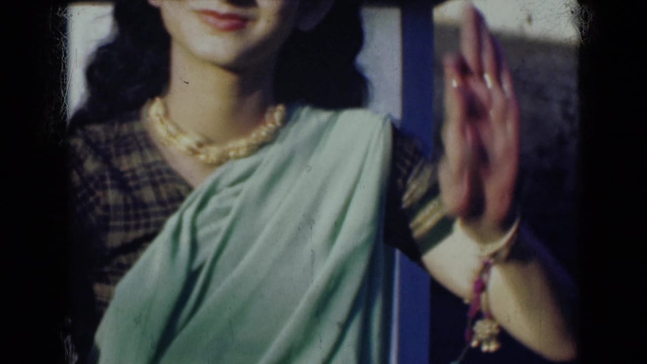 1947 India 8mm frame showing a woman in a light green sari with necklace and jewelry, smiling slightly as one hand is held upright.