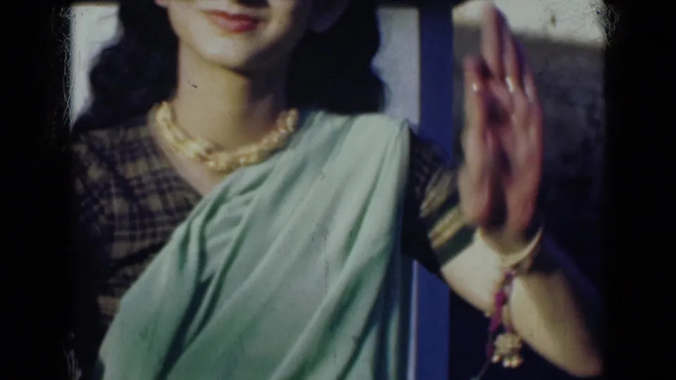1947 India 8mm frame showing a woman in a light green sari with necklace and jewelry, smiling slightly as one hand is held upright.