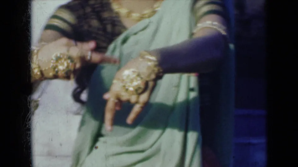 1947 India 8mm frame showing a woman in a light green sari with gold bangles, rings, and hand ornament forming a dance gesture.