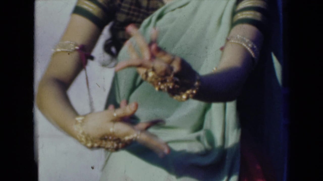 Jewelry-covered hands form a traditional dance gesture against a sari.