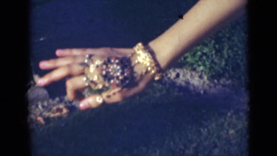 Close 8mm frame from India in 1947 showing an extended hand with gold jewelry and rings near green patterned cloth.