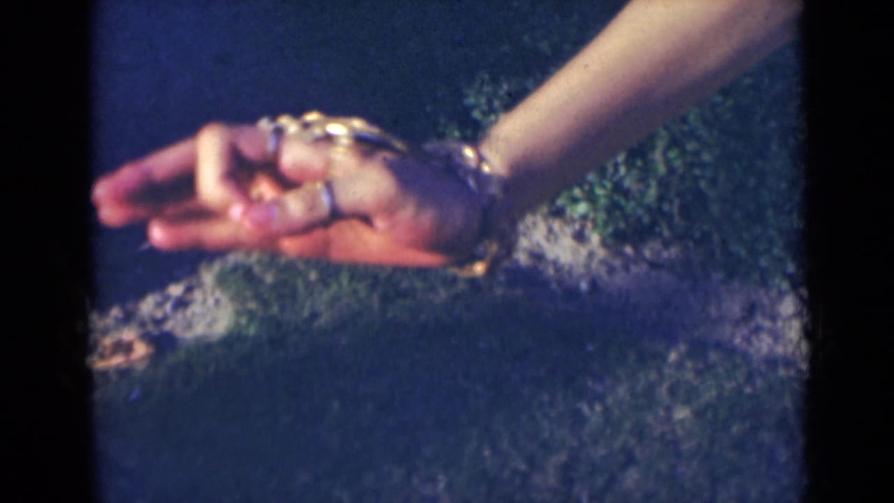 Woman's hand with rings and bracelets held palm-up against dark outdoor ground.