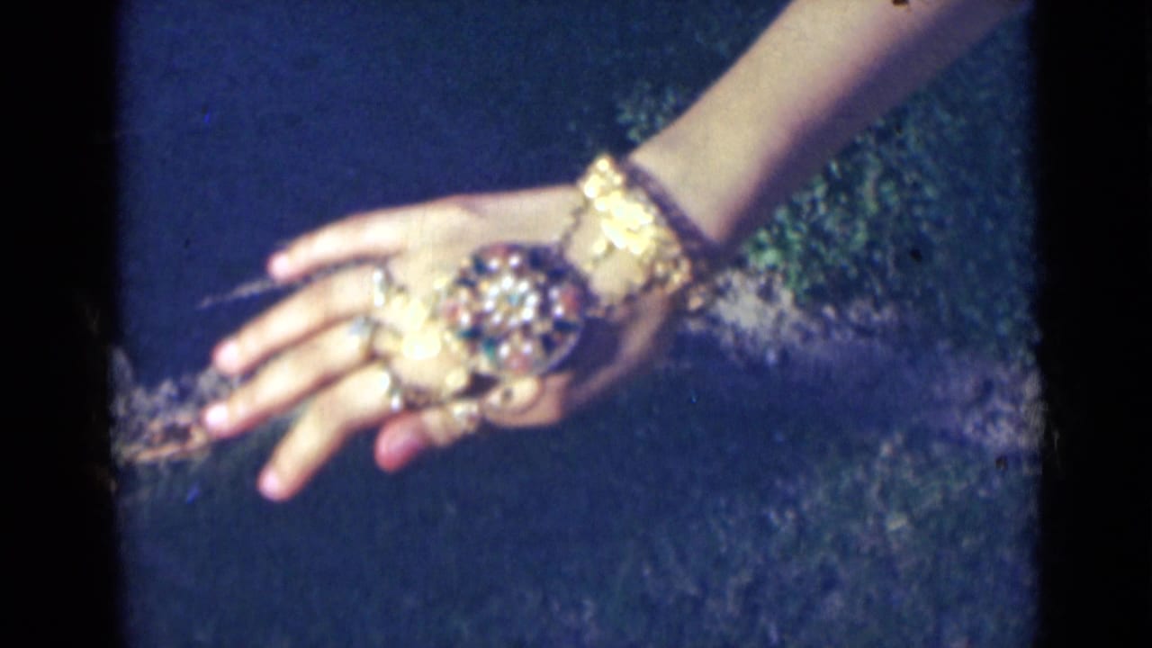 The back of a woman's hand fills the frame, with a large decorative ring and gold-colored wrist jewelry visible in 1947 India footage.
