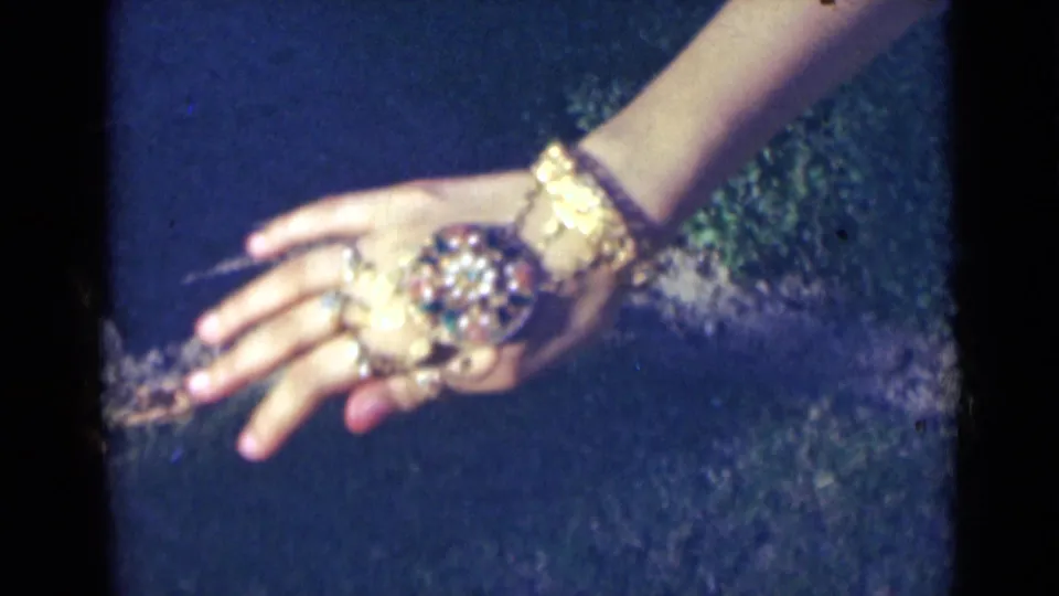 The back of a woman's hand fills the frame, with a large decorative ring and gold-colored wrist jewelry visible in 1947 India footage.