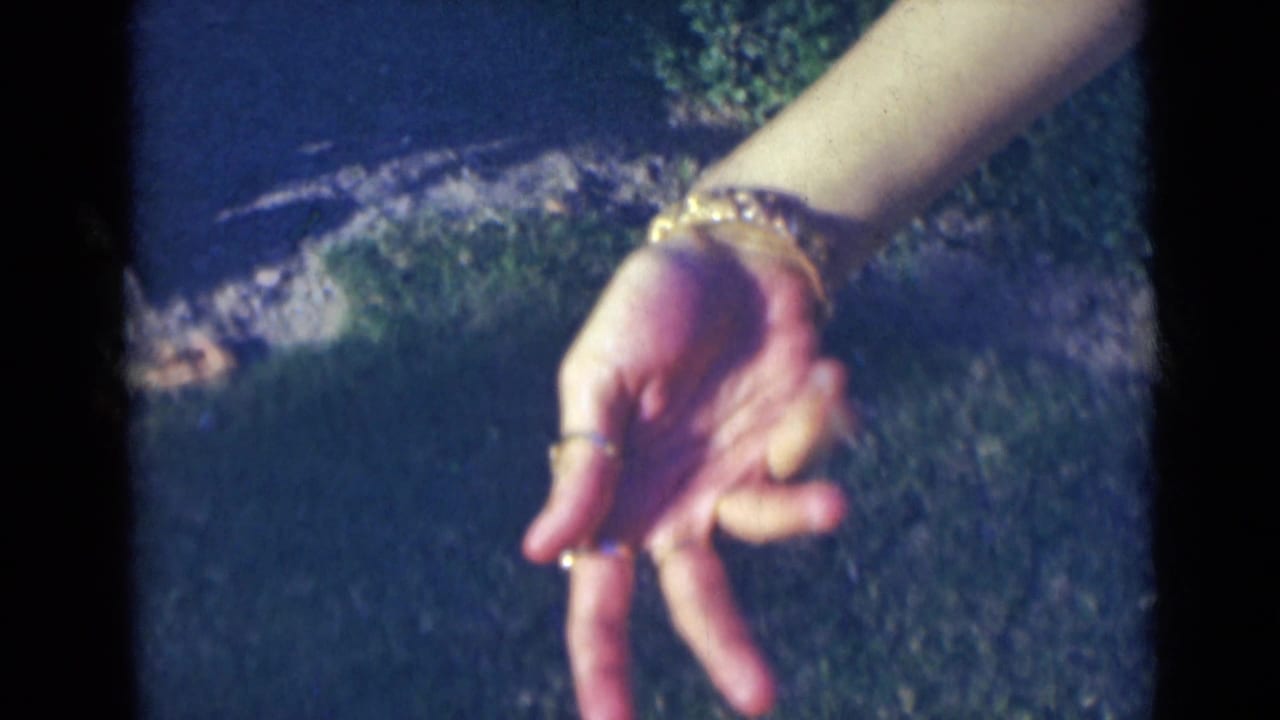 A close 1947 India frame shows a woman's bracelet-covered wrist and ringed fingers forming a loose, expressive gesture outdoors.