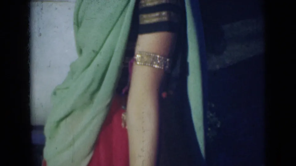 Partial view of a woman in green and red traditional attire, with a gold-toned arm ornament visible in 1947 India footage.