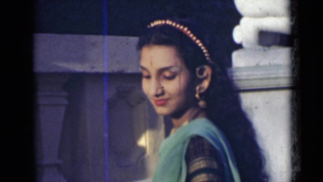 Woman in a green sari looking downward beside a white stone structure.
