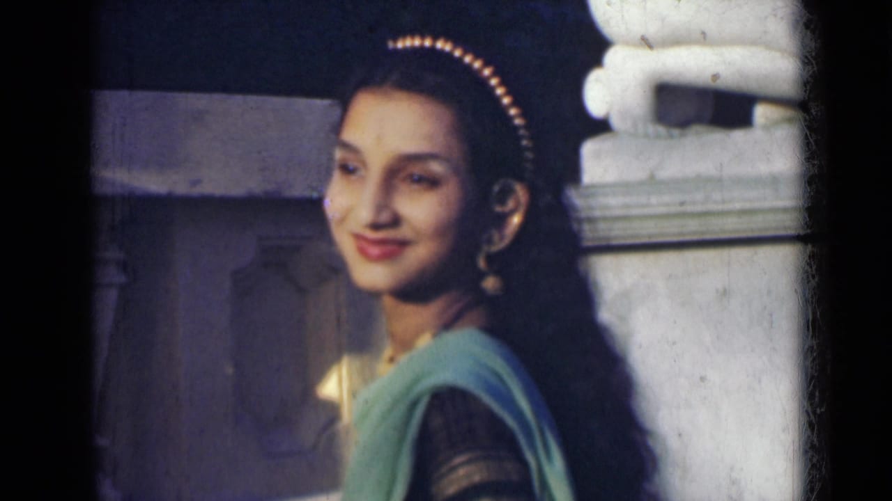 An adult woman in a green sari smiles toward the camera near a pale stone architectural feature in India, dated 1947 by metadata.