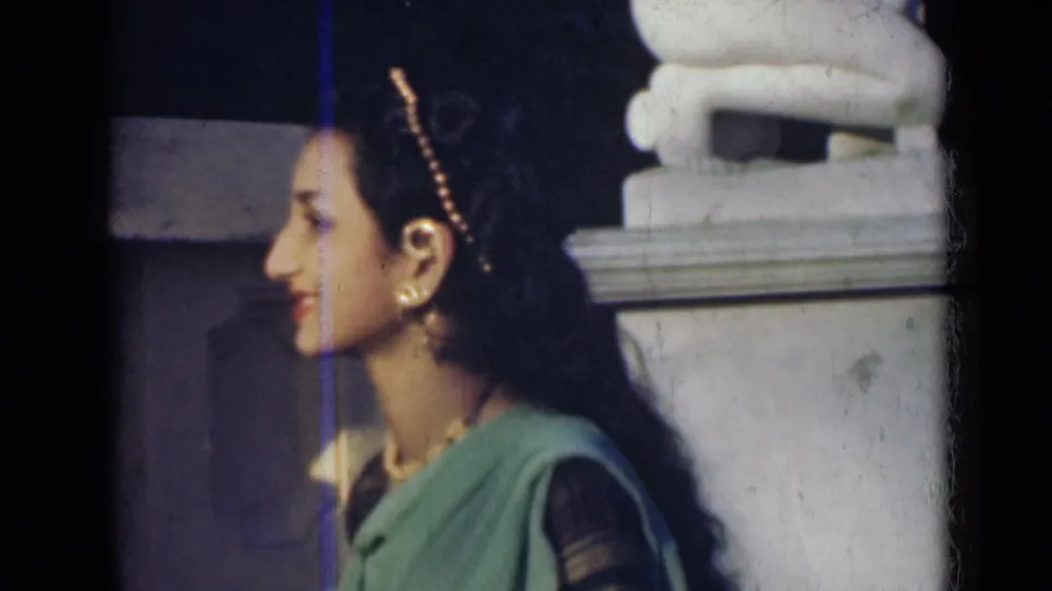 Profile view of an adult woman in a green sari and jewelry standing beside a white stone structure in 1947 India footage.