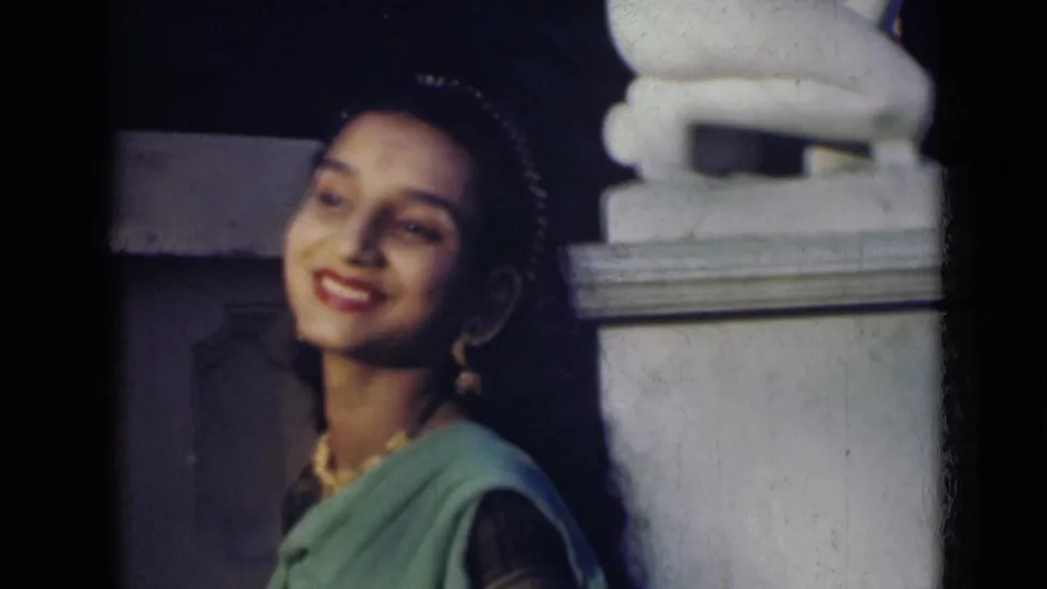 An adult woman in a green sari laughs beside a white stone structure in a short 1947 India home-movie shot.