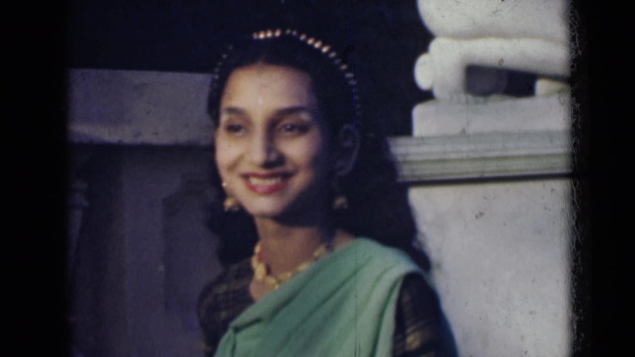Young woman in India, 1947, smiling toward the camera while wearing a green sari, dark blouse, necklace, earrings, and head ornament.