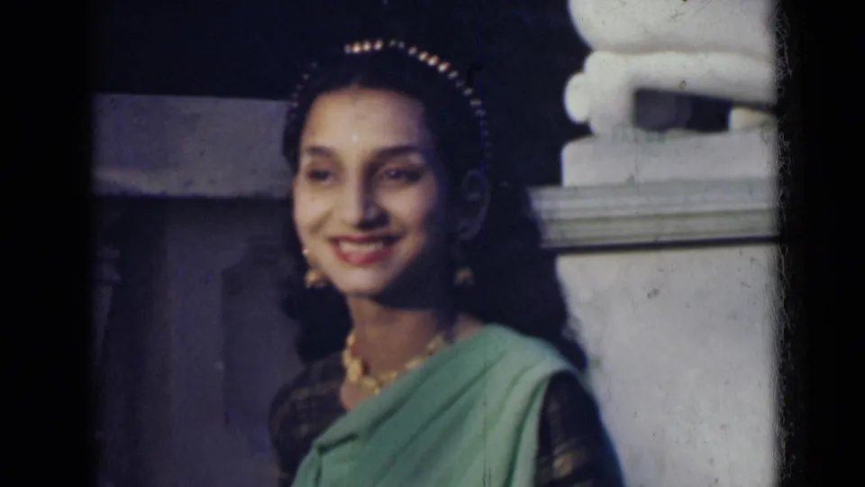 Young woman in India, 1947, smiling toward the camera while wearing a green sari, dark blouse, necklace, earrings, and head ornament.