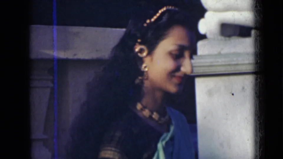 Young woman in India, 1947, looks down with a slight smile, showing her earrings, necklace, hair ornament, and draped green sari.
