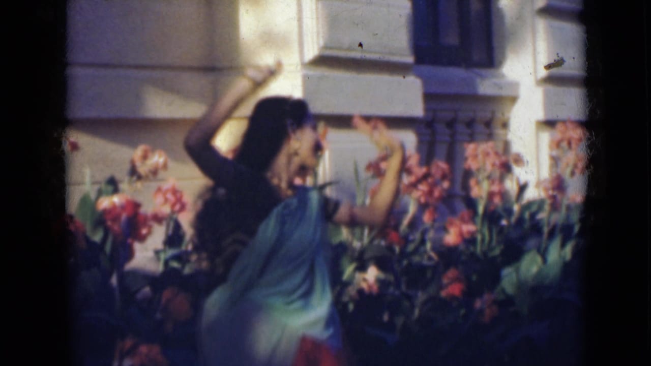 Woman in a sari raises her arms while dancing among garden flowers.