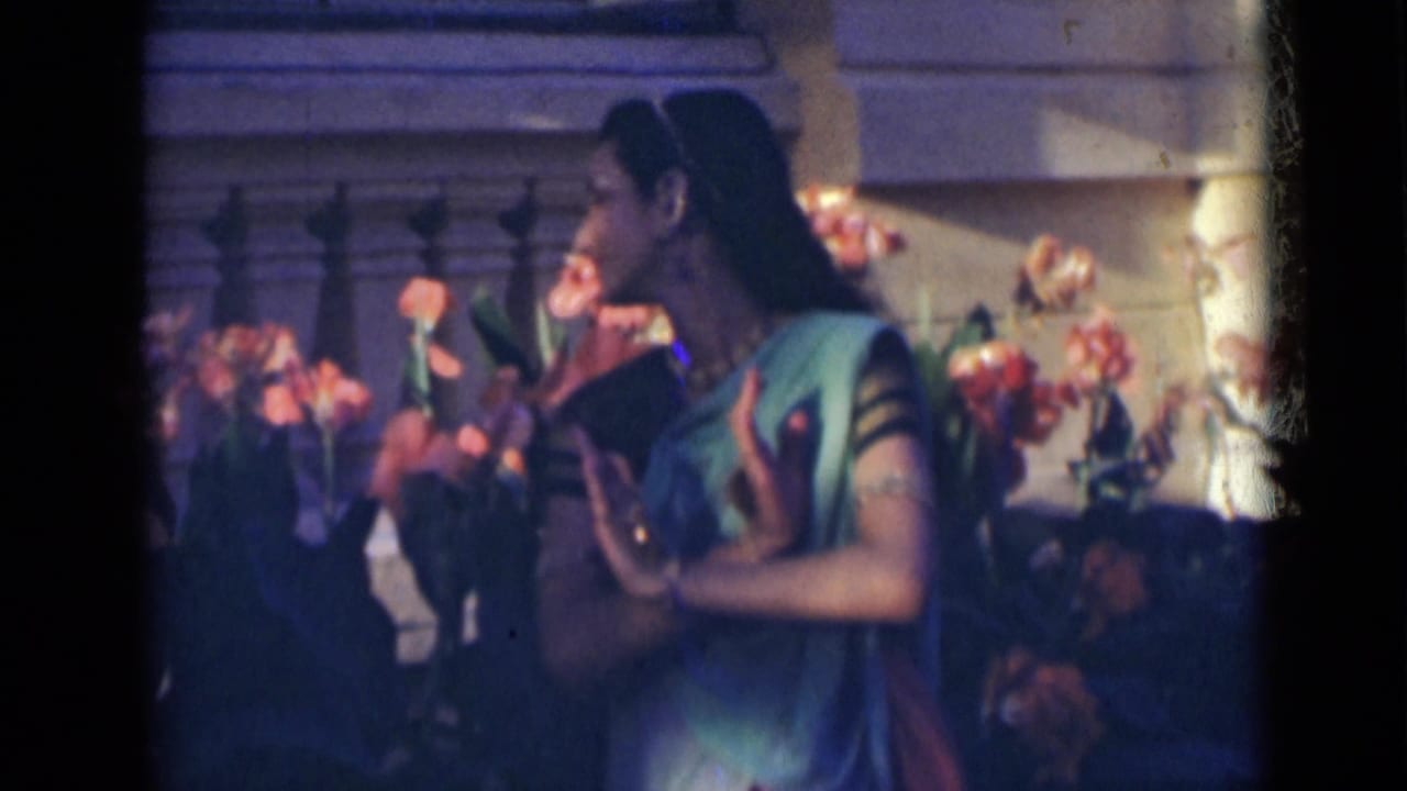 Woman in a sari turns in profile with one hand raised near flowers.