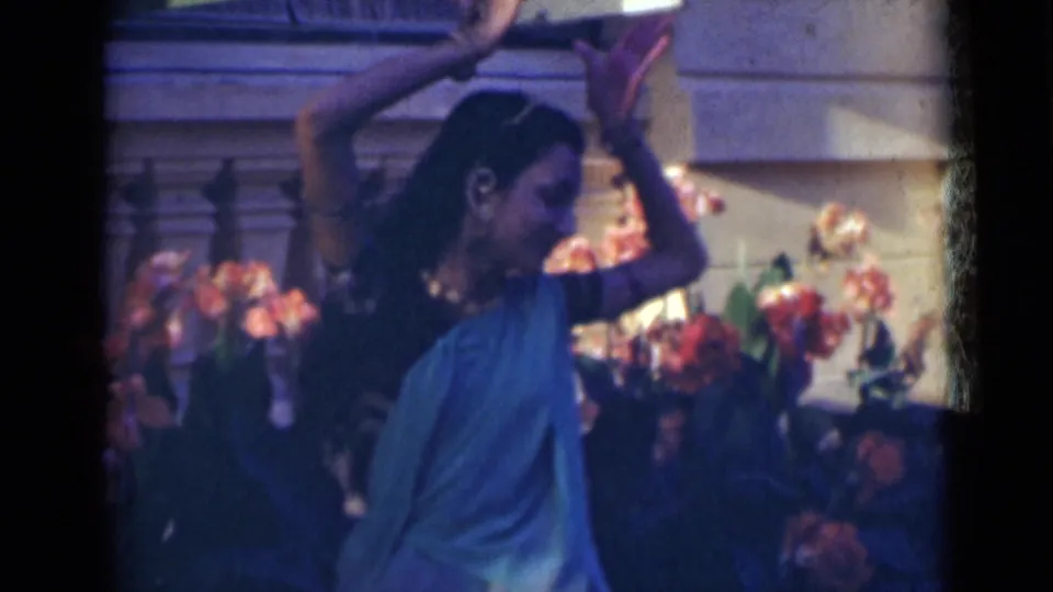 Side view of the dancer in teal clothing with both arms raised, filmed on 8mm in India in 1947.