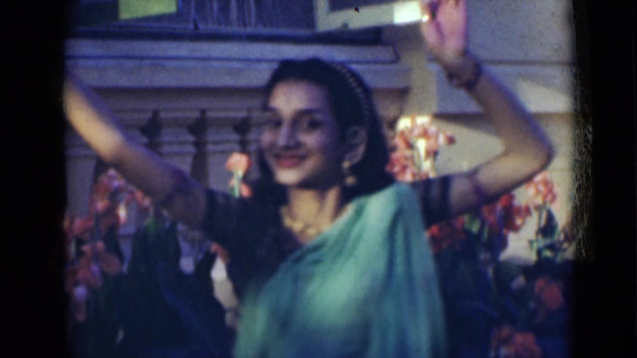In 1947 India home-movie footage, a young woman in a green sari and jewelry raises her arms during an outdoor dance.