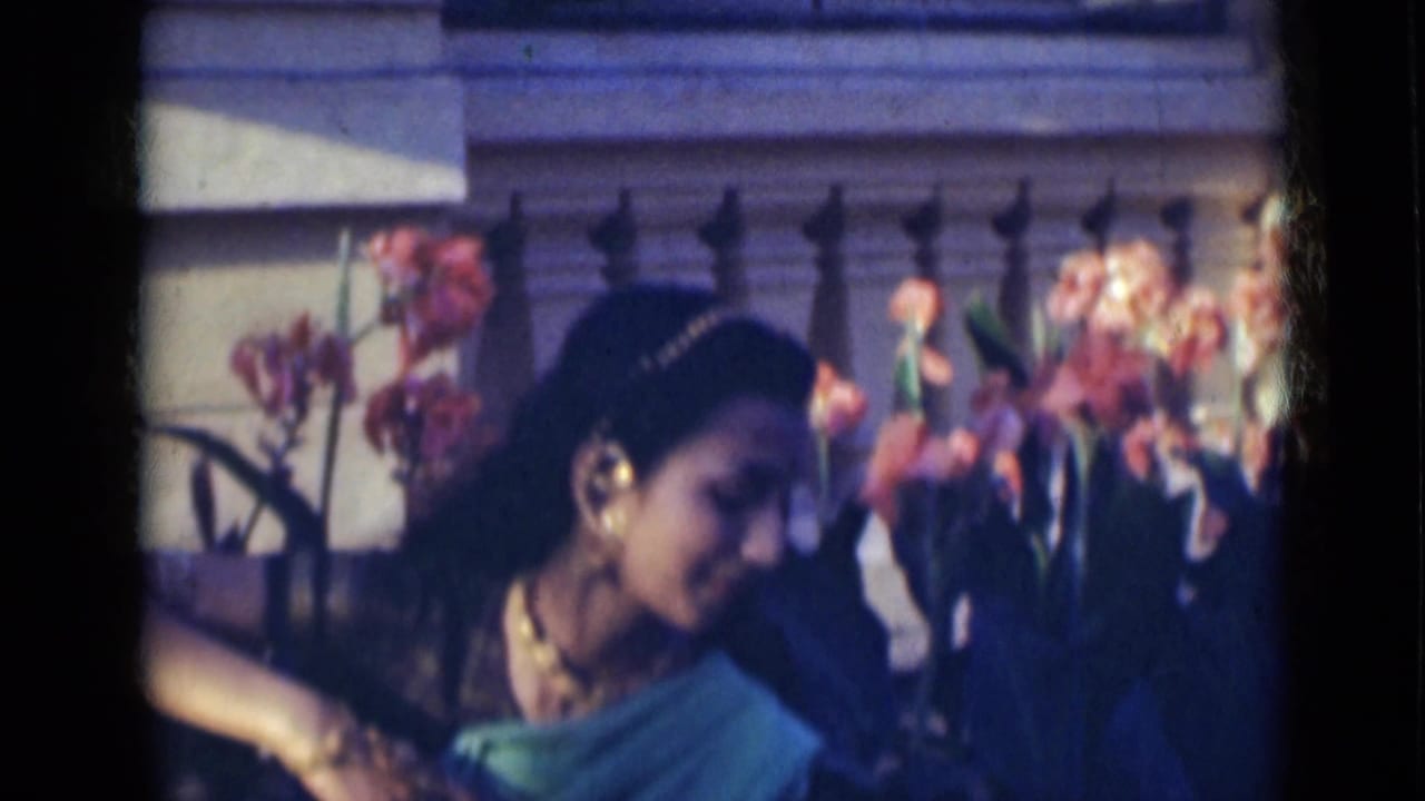 Young woman bends her head and extends an arm while dancing near flowers.