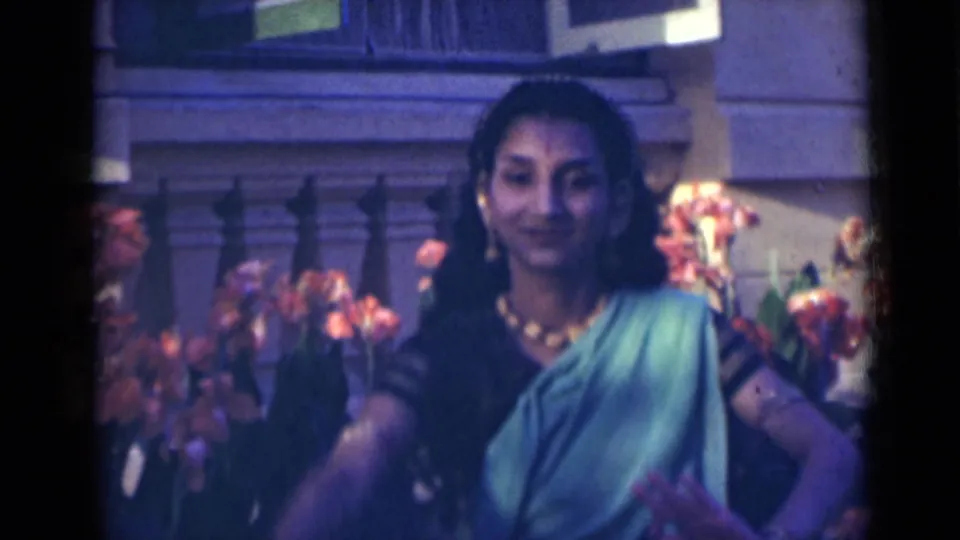 The dancer faces the camera in a green sari, with jewelry visible and flowers behind her in the 1947 India footage.