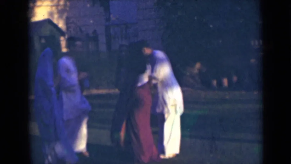 Adults in traditional attire appear to pause and interact outdoors in India, with soft 8mm color and dusk exposure.