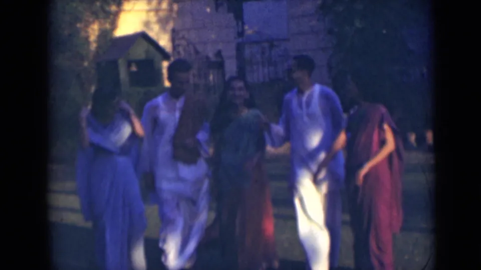 The adults approach the camera in soft 8mm footage, walking closely together in traditional Indian clothing.