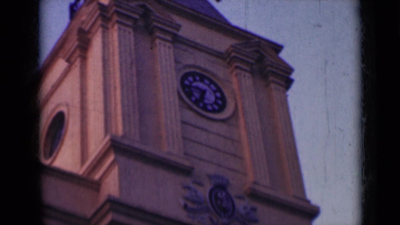 1947 India 8mm frame showing an upward view of an ornate clock tower with a round clock face and classical facade details.