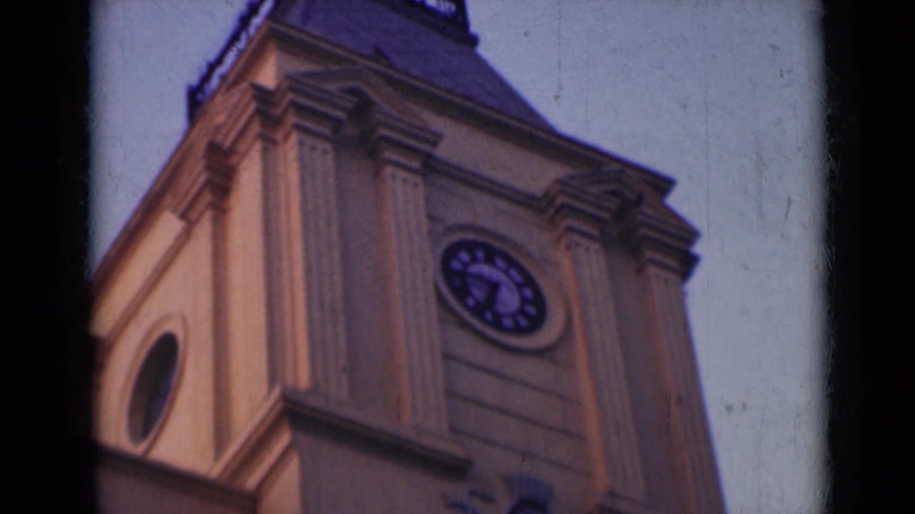 1947 India 8mm frame of the tower's upper section, including the clock face, columns, dark roofline, and blue evening sky.