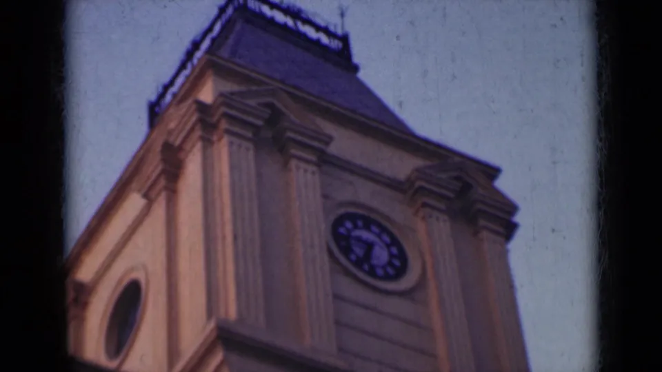 1947 India 8mm frame with a low-angle view of the ornate tower, showing an arched side opening, clock face, and columned facade.