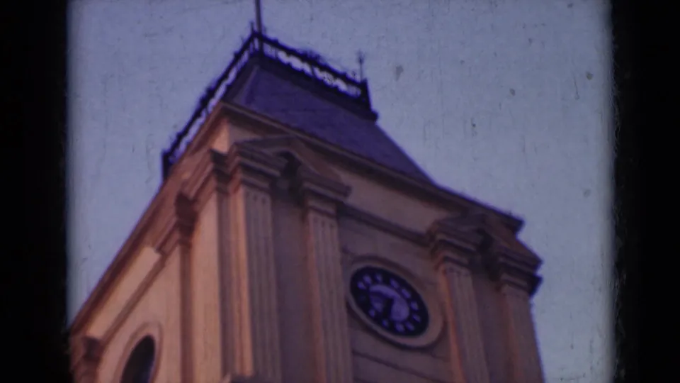 1947 India 8mm frame showing the upper clock tower with its round clock face, dark roof, roof railing, and ornate column details.