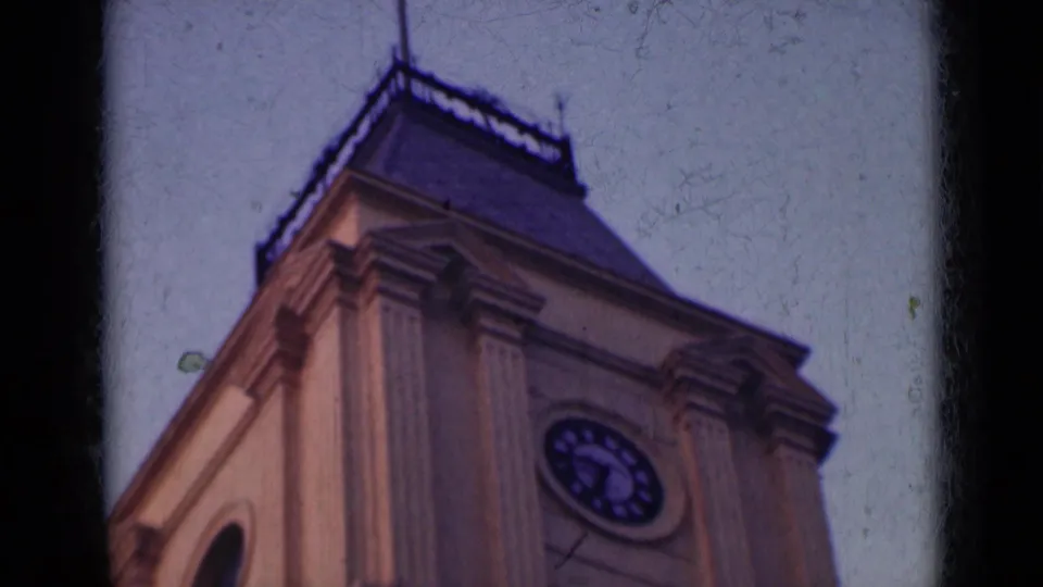 1947 India home-movie frame showing the upper portion of a clock tower or civic building, viewed from a low angle.