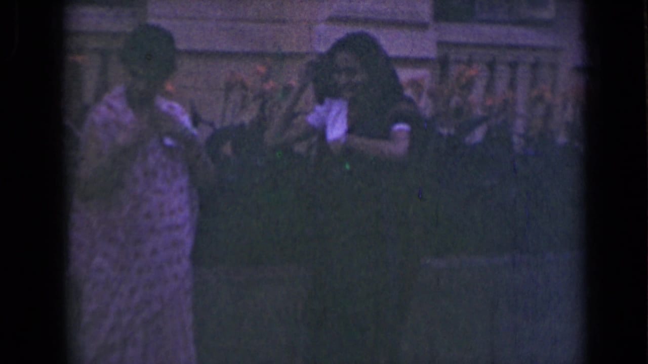 Two women stand outdoors near a stone building, adjusting draped head coverings.