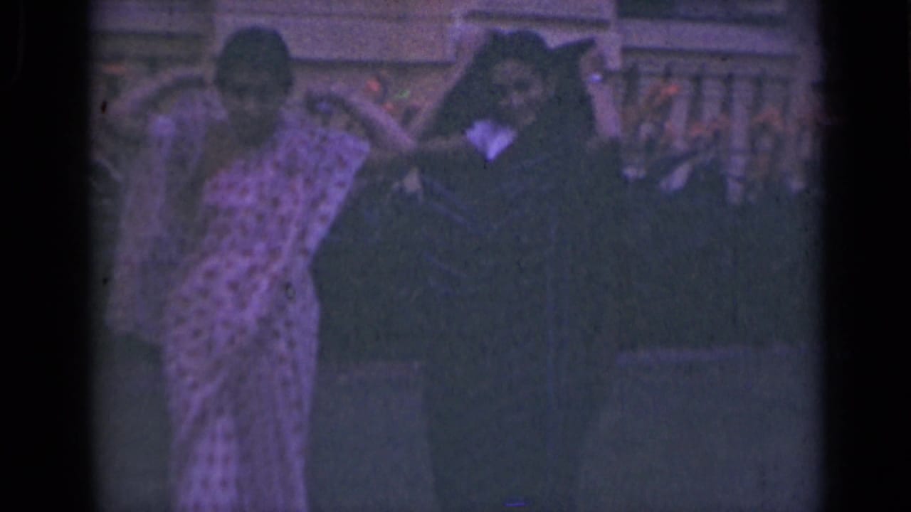 Two women in traditional attire appear to adjust sari fabric and head coverings near a stone exterior in India.