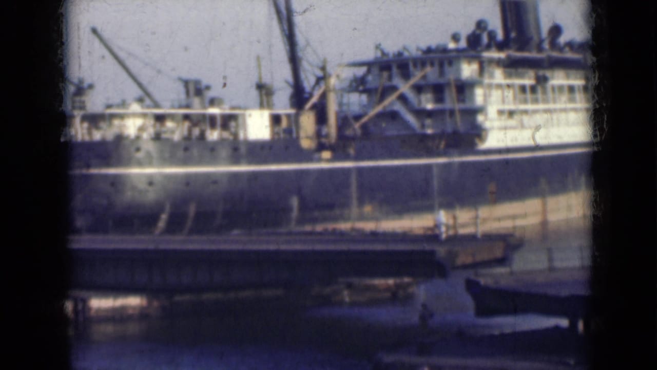 The docked ship remains framed across the water, with a bridge in the foreground and port structures behind it in 1947 India footage.