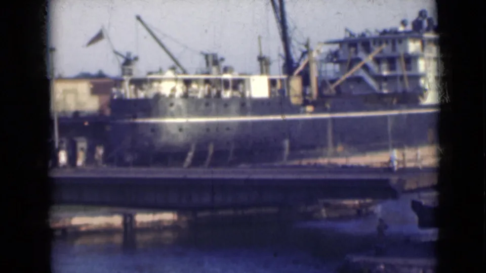 A closer view of the ship's dark hull and white deck levels appears beyond the bridge, with port equipment and water visible in India.