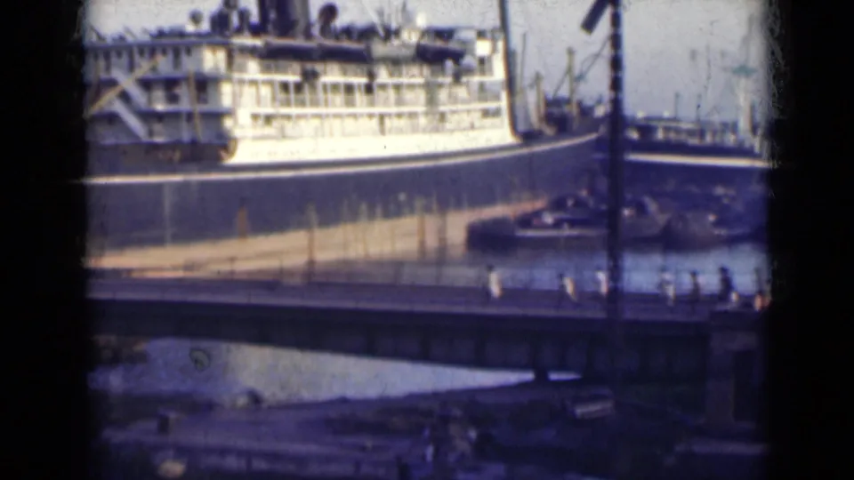 The ship is partly obscured by the foreground bridge, where small distant people are visible near the water at an Indian port in 1947.