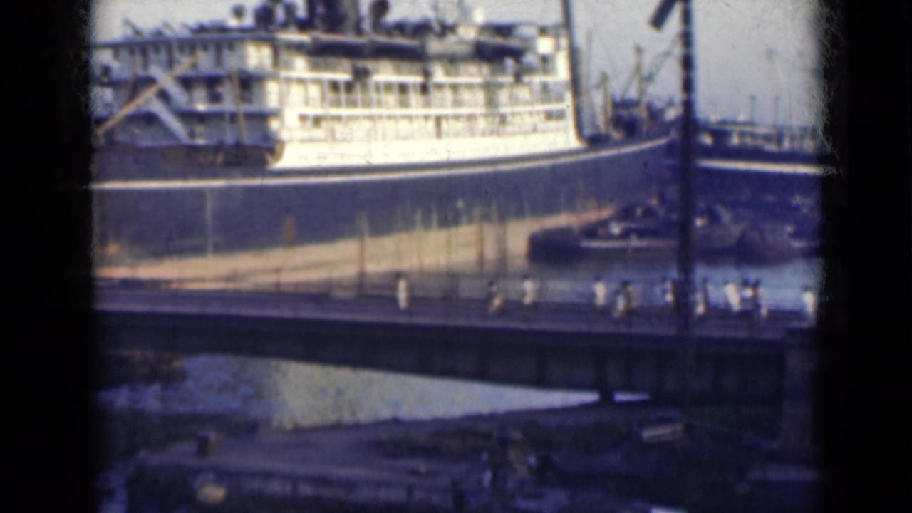 Large passenger ship behind a bridge with small pedestrians crossing in the foreground.