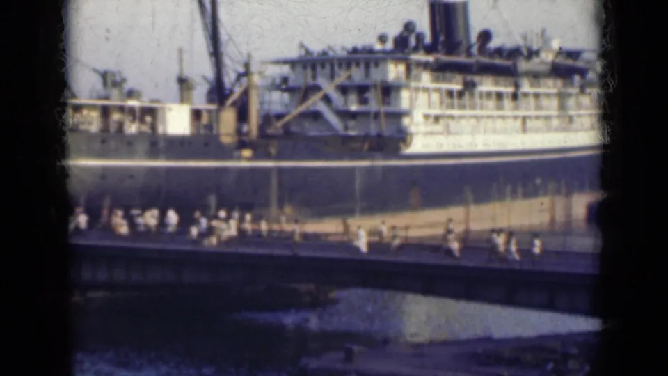 Final 8mm frame showing the docked ship in India with pedestrians crossing a bridge and water visible below.