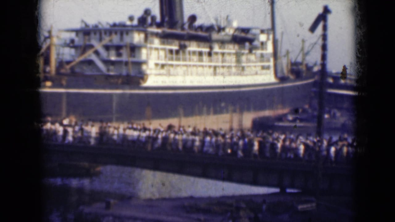 1947 India frame with a crowd walking along a dockside bridge below the side of a large ship.