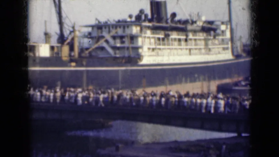 1947 India frame showing people moving along a dockside bridge toward or beside a large ship.