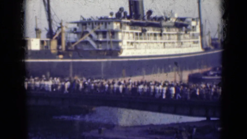 1947 India 8mm frame with a large passenger vessel and a packed line of people crossing the foreground bridge.