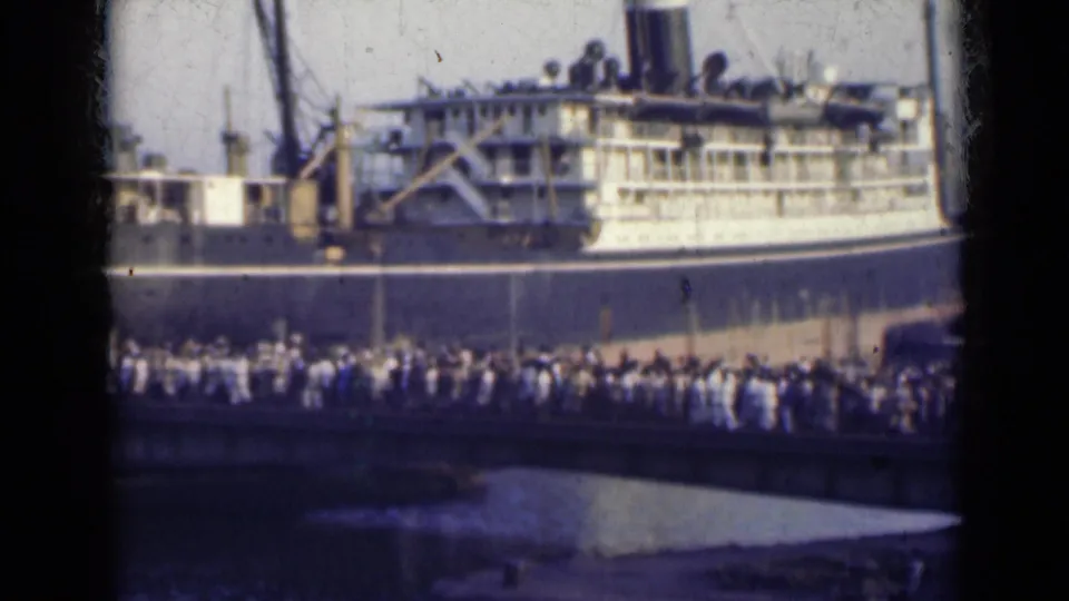 Faded 8mm frame from 1947 India showing people packed along a bridge in front of a docked ocean liner.