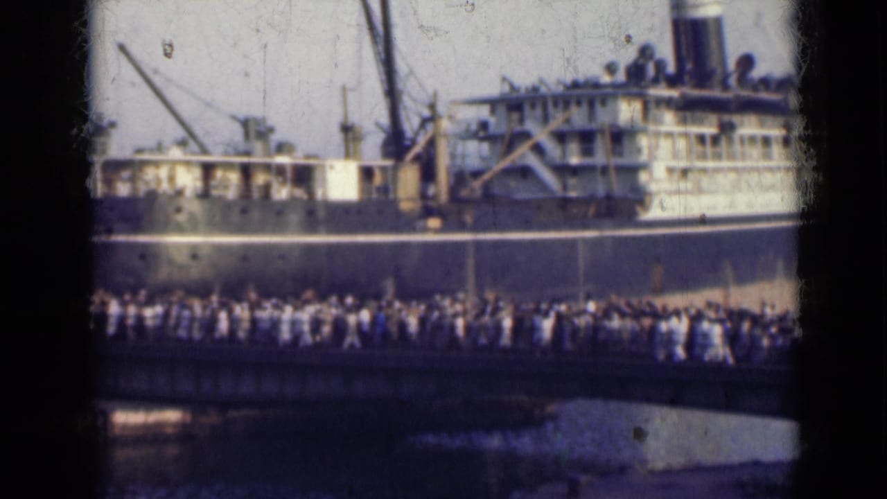1947 India home-movie frame showing people moving across a bridge in front of a dark-hulled passenger ship.
