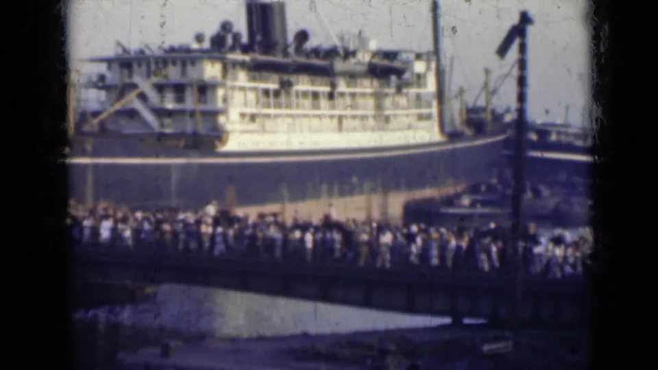 Faded 8mm frame from 1947 India showing a ship at the waterfront with a dense crowd crossing the bridge below.